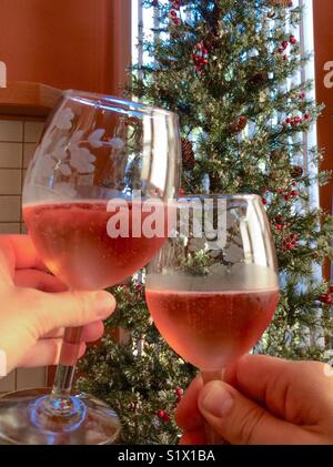 Un toast de vacances avec vin rosé mousseux, avec l'arbre de Noël décoré à l'arrière-plan Banque D'Images