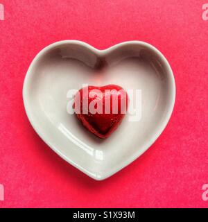 Coeur rouge en chocolat dans un plat de céramique blanche sur fond rouge Banque D'Images