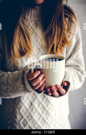 Portrait d'une jeune fille blonde dans un confortable pour homme tenant une tasse de café chaud sur ses mains pour garder au chaud Banque D'Images