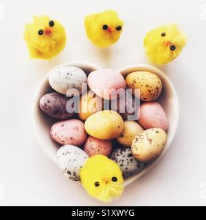 Les oeufs de Pâques en chocolat dans un plat en forme de coeur en céramique avec de petits poussins de Pâques Banque D'Images
