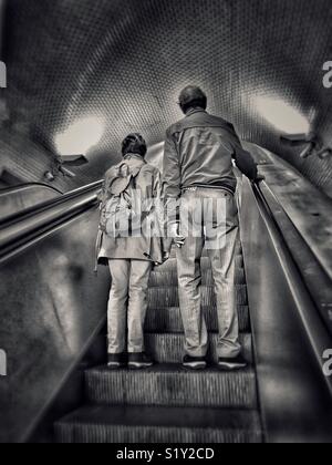 2 personnes - peut-être mariée ? Peut-être des amis ? - Voyage vers le haut ensemble sur un escalator. Qui sont-ils ? Où vont-ils ? Qui s'en soucie ? Une image avec de multiples possibilités d'utilisation. Photo © - COLIN HOSKINS. Banque D'Images