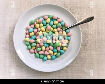 Bol de chocolat enrobés de sucre coloré mini-oeufs, avec une cuillère. Un amusant mais pas-si-petit-déjeuner de Pâques en bonne santé. Banque D'Images