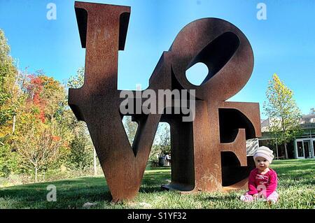 Un bébé se trouve à la base de l'amour de Robert Indiana la sculpture à l'entrée nord de la Crystal Bridges Museum of American Art. La sculpture est l'un des plus populaires dans la collection du musée. Banque D'Images