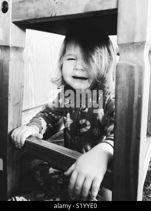 Image en noir et blanc de bébé fille pleurer sous un tabouret en bois Banque D'Images