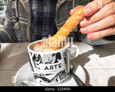 Femme un biscuit tremper dans une tasse de cappuccino dans un café, midsection view Banque D'Images