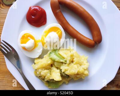 Une paire de saucisses de Vienne, oeufs, mayonnaise, ketchup et salade de pommes de terre sur une plaque blanche Banque D'Images