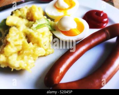 Une paire de saucisses de Vienne, oeufs, mayonnaise, ketchup et salade de pommes de terre sur une plaque blanche Banque D'Images