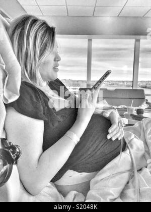 Femme enceinte dans l'attente de l'hôpital pour accoucher alors que sur son iPhone Banque D'Images