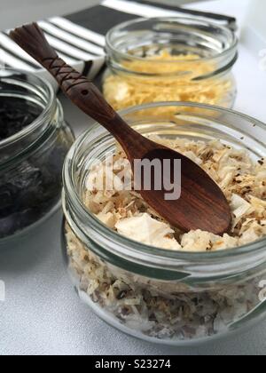 Gros plan d'un bocal en verre avec champignons aromatisés et une cuillère en bois. Deux autres bols sont volontairement un peu en dehors de l'accent principal derrière le bocal en verre. Banque D'Images