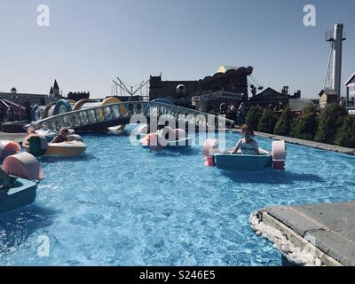 Enfants jouant sur des mini-bateaux propulsés à la main à un parc à thème sur une belle journée chaude. Banque D'Images