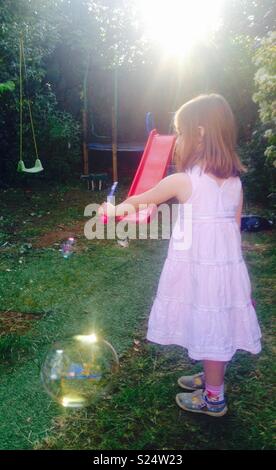 Petite fille faisant des bulles dans le jardin avec un faible soleil du soir. Banque D'Images