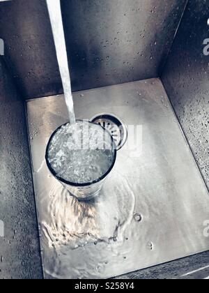 Remplissage d'eau du robinet et s'échappant d'un grand verre dans un évier en acier inoxydable Banque D'Images