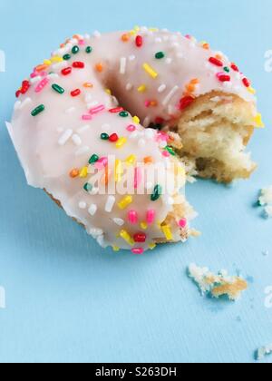 Un livre blanc saupoudrer avec un donut morsure hors de celui-ci sur un fond bleu. Banque D'Images