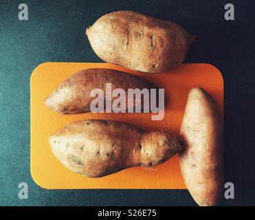 Quatre patates sur une petite planche à découper orange et vert foncé du comptoir Banque D'Images