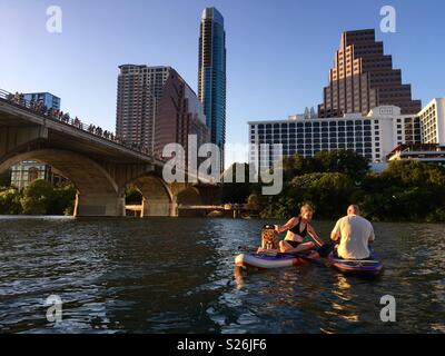 Un couple et le flotteur sur paddle boards sur Ladybird Lake à Austin, Texas, comme une foule se rassemble sur le pont de l'Avenue des congrès pour regarder une colonie de chauves-souris apparaissent. Banque D'Images