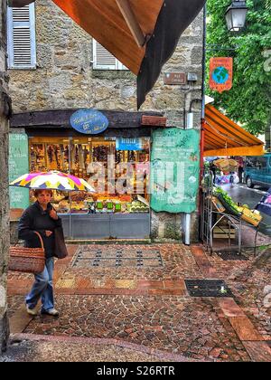 Un jour de pluie à Figeac, France. Une petite ville de marché au coeur de la département du Lot. Une dame est shopping pour les fruits et légumes, l'exécution d'un parasol et de paniers traditionnels. Banque D'Images