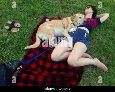 Femme couchée avec son chien labrador blond sur couverture de pique-nique et de l'herbe en été Banque D'Images