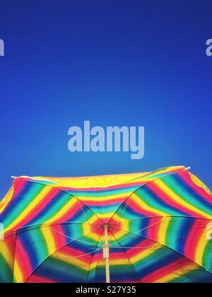 Brillamment colorés et lumineux parapluie de plage contre un bleu clair d'un ciel d'été. Banque D'Images