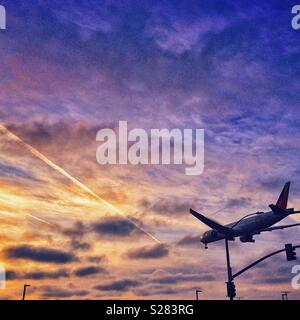 Les terres d'un avion comme le soleil se couche contre un ciel nuageux à LAX Airport en Californie Banque D'Images