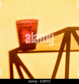 Ombre d'un verre en plastique transparent rouge sur un verre surmonté metal pattes table créer une image abstraite. Banque D'Images