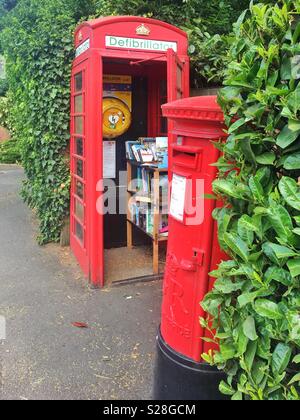 Une boîte de téléphone rouge transformée en une bibliothèque et defribillator, et un pilier rouge post box ou box dans le village de Dorney, dans le Berkshire, Angleterre Banque D'Images