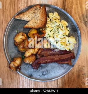 Une vue de dessus d'un petit-déjeuner d'œufs brouillés, bacon, pommes de terre et de pain grillé sur une plaque en métal rustique Banque D'Images