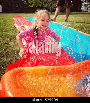 6 ans, fille, glissant sur l'eau en plastique à l'extérieur jouets glisser sprinkleur Banque D'Images
