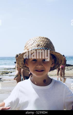 Boy on beach wearing straw hat avec derrière lui la mer Banque D'Images