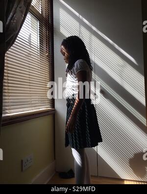 Fille dans un kilt debout dans le soleil à travers une fenêtre Banque D'Images