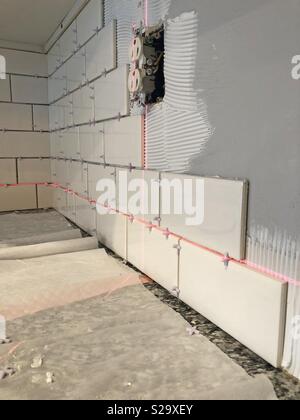 L'installation de carreaux de mur blanc au-dessus d'un comptoir de la cuisine en utilisant un niveau laser autour d'une prise électrique avec copie espace. Banque D'Images