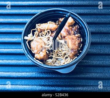 La cuisine chinoise, l'orange poulet et nouilles chow mein dans un bol noir avec un tablier noir assis sur le hayon d'un camion prêt à être mangé. Banque D'Images