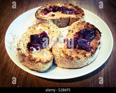 Trois tranches de pain complet, beurre et confiture de fraise sur toast sur une assiette blanche Banque D'Images