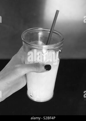 Le noir et blanc photo d'une main de femme tenant un verre de lait avec une paille Banque D'Images