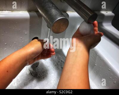 Un enfant se lave les mains sous un robinet dans les toilettes. Banque D'Images