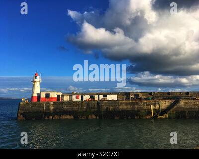 Leuchtturm et bâtiments peints en rouge et blanc sur le bord du port de Newlyn Cornwall, ciel bleu avec un grand nuage blanc et gris Banque D'Images