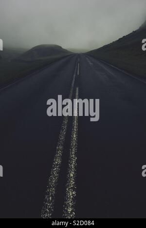 Une route sombre avec des lignes blanches dans la pluie et nuage de la sombre paysage de l'Islande Banque D'Images