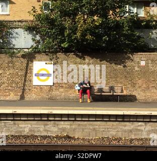 Tandis que la lecture de l'homme était assis sur un banc à la plate-forme ferroviaire Banque D'Images