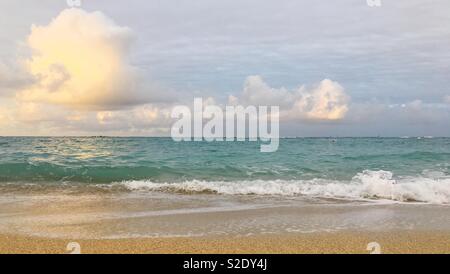 L'écrasement de l'onde sur plage de sable avec des nuages au-dessus sur une sereine au petit matin. Banque D'Images