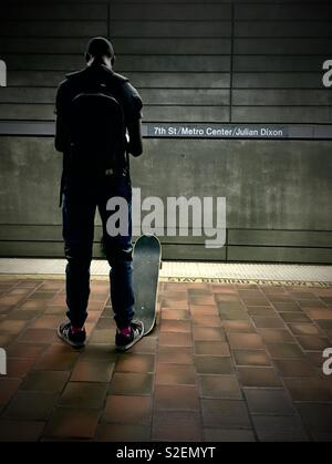 Young African American man attend avec skateboard pour la Metro train sur la plate-forme à la 7th Street Metro Center dans le centre-ville de Los Angeles Banque D'Images