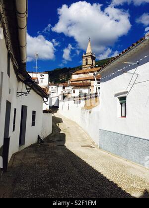 Jusqu'à un étroit couloir ou de rue dans un village de l'Andalousie en Espagne par le biais de la vieille église et maisons blanches au sommet de la colline Banque D'Images