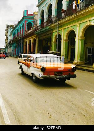 Conduite de voiture orange vif coloré passé bâtiments coloniaux à La Havane Cuba Banque D'Images