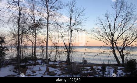 Dawn pastel sur le lac Supérieur avec la silhouette des arbres et de la neige sur la rive en premier plan Banque D'Images