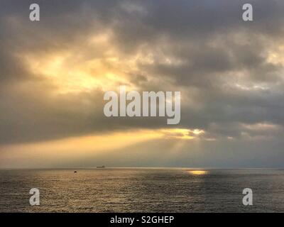 Sunburst par d'épais nuages sur la mer avec des rayons crépusculaires. Banque D'Images