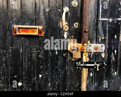 Vieille porte fermée avec de la peinture noire et une boîte aux lettres. Banque D'Images