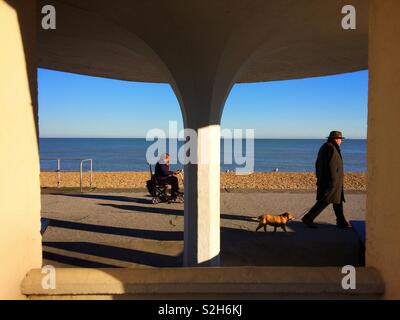 Une femme sur un scooter de mobilité et un homme qui marchait le long de la promenade de la plage de Deal, Kent, UK Banque D'Images