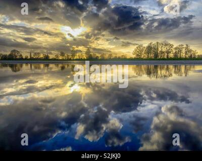 Coucher de soleil spectaculaire et coloré dans un ciel nuageux avec des nuages noirs et blancs reflétés sur la surface de l'eau d'une flaque d'eau après la pluie Banque D'Images