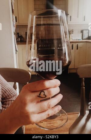 Femme tenant un verre de vin rouge dans la main avec coeur tattoo Banque D'Images