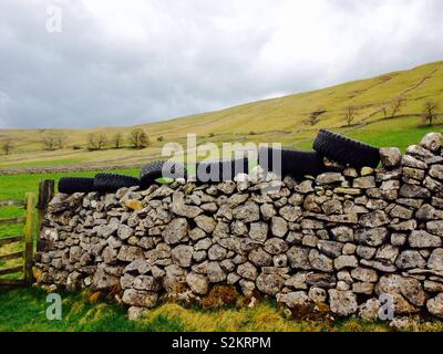 Les vieux pneus sur un mur de pierres sèches Banque D'Images