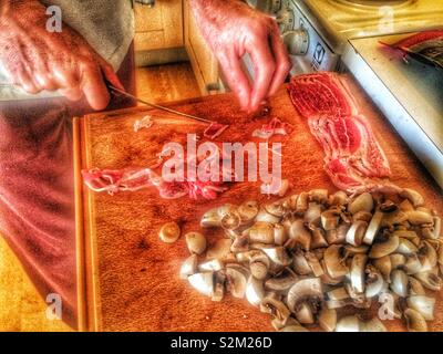 Man slicing bacon et champignons sur sortir à découper dans un Swdish accueil cuisine, Suède, Scandinavie Banque D'Images