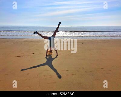 Jeune femme faisant la roue sur une plage de sable. Banque D'Images
